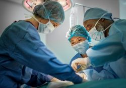 Team of doctors are performing surgery on a patient at hospital. Multi-ethnic surgeons are operating patient in emergency room. They are wearing blue scrubs.